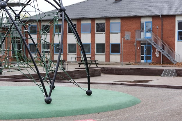 A well-maintained school playground with soft landing surfaces under the equipment, supervising teachers actively monitoring the children playing, and clear safety signs posted around the area.