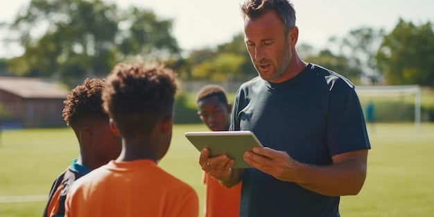 A coach using a tablet on the sidelines of a youth soccer game. The tablet displays real-time player statistics and analytics. The coach is pointing to the screen while talking to a player, demonstrating the use of data to provide feedback.
