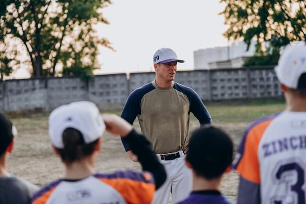 A coach is demonstrating the correct throwing technique to a young baseball player. The coach is kneeling to be at eye level with the player and providing clear, concise instructions.