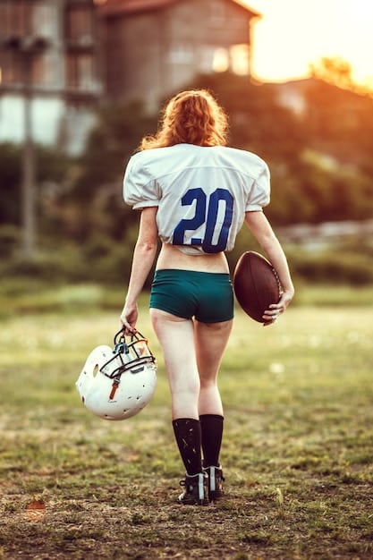 A close-up shot of a female flag football player's hands gripping the football, preparing for a pass. The focus is on the texture of the ball and the athlete's determined expression. The background is slightly blurred, showing other players in action.