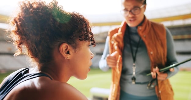 A college coach talking to a high school athlete during a break in a summer recruitment camp. The coach should be pointing to a play diagram or providing tactical advice. The image should convey mentorship, guidance, and a focused evaluation.