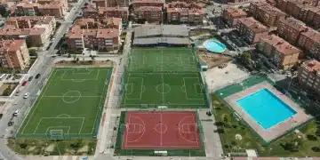 Vista aérea de un moderno complejo deportivo local en España, destacando campos de fútbol, canchas de baloncesto y piscina.