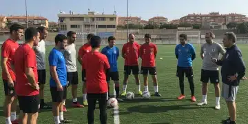 Deportistas de ligas locales en España recibiendo instrucciones de seguridad en un campo deportivo soleado.